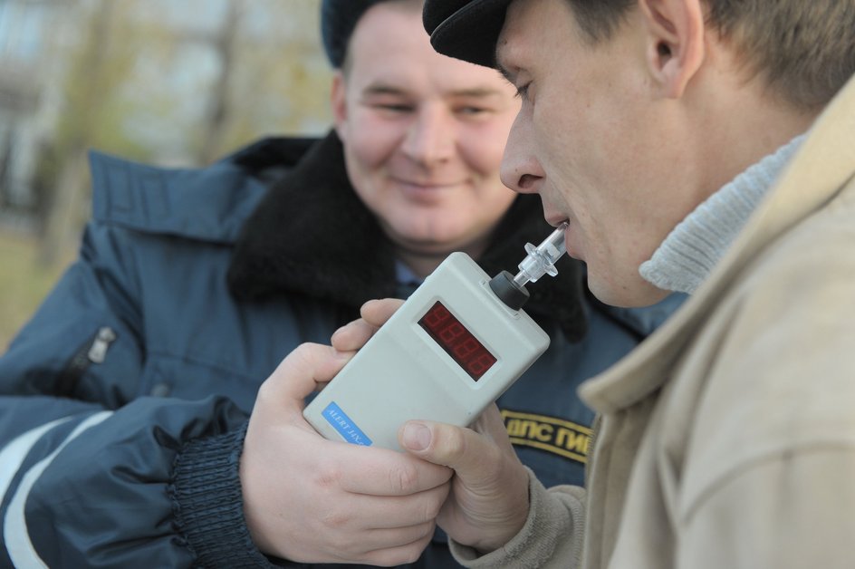 Сотрудник ГИБДД проверяет водителя автомобиля алкотестером на содержание алкоголя в крови