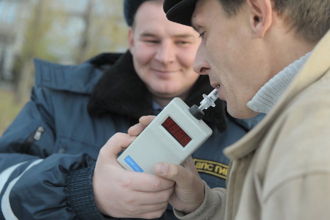 Сотрудник ГИБДД проверяет водителя автомобиля алкотестером на содержание алкоголя в крови Сотрудник ГИБДД проверяет водителя автомобиля алкотестером на содержание алкоголя в крови