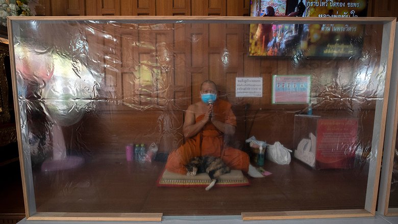 Буддийский монах молится за защитной пластиковой перегородкой во время Тайского Нового года в храме Самьяна Нари в Бангкоке