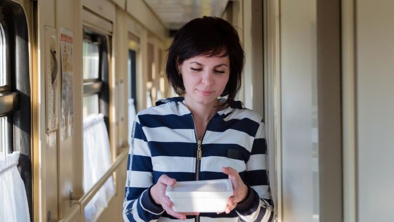 Женщина путешествует по России в поезде, в руках с контейнером с едой быстрого приготовления.