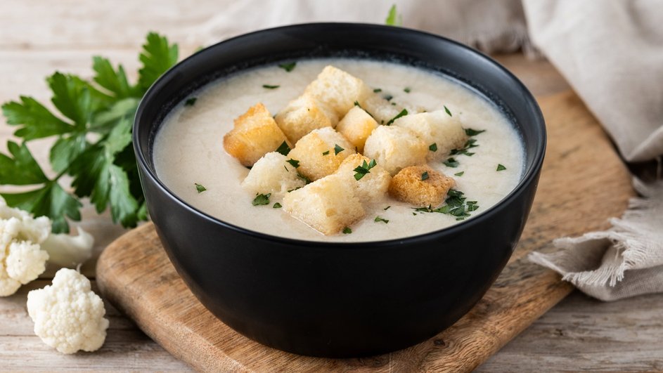 Тарелка супа из сушеных белых грибов с сыром и гренками стоит на доске рядом с зеленью