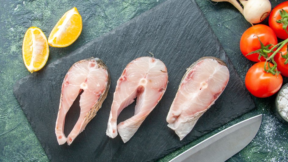 Кусочки сырой рыбы лежат на доске рядом с помидорами, ножом и дольками лимона Кусочки сырой рыбы лежат на доске рядом с помидорами, ножом и дольками лимона