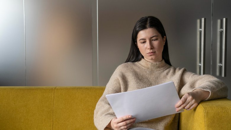 Женщина сидит на диване и читает о циклической безработице на листах. Женщина сидит на диване и читает о циклической безработице на листах.