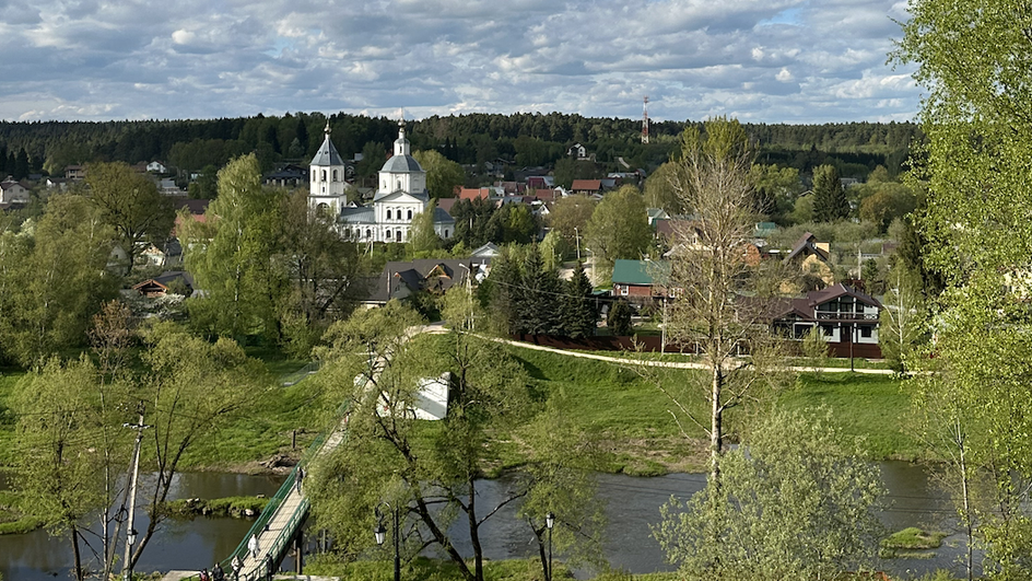 Панорама города с церковью, мостом и деревянными домами на фоне леса.