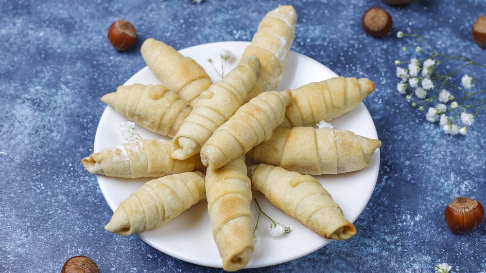 Песочные рогалики лежат на тарелке рядом с орехами Песочные рогалики лежат на тарелке рядом с орехами
