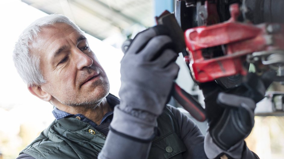 Мужчина в перчатках меняет тормозные колодки на автомобиле