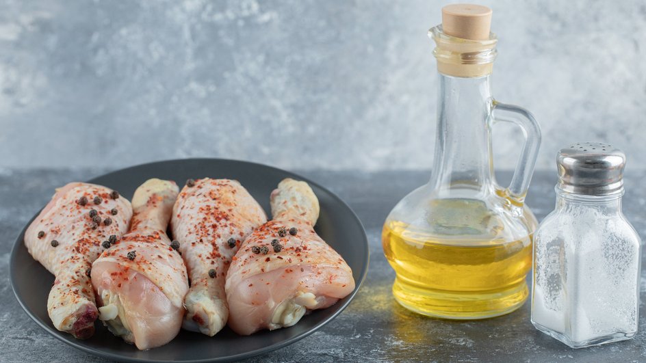 Маринованная курица лежит на тарелке рядом с оливковым маслом и солью