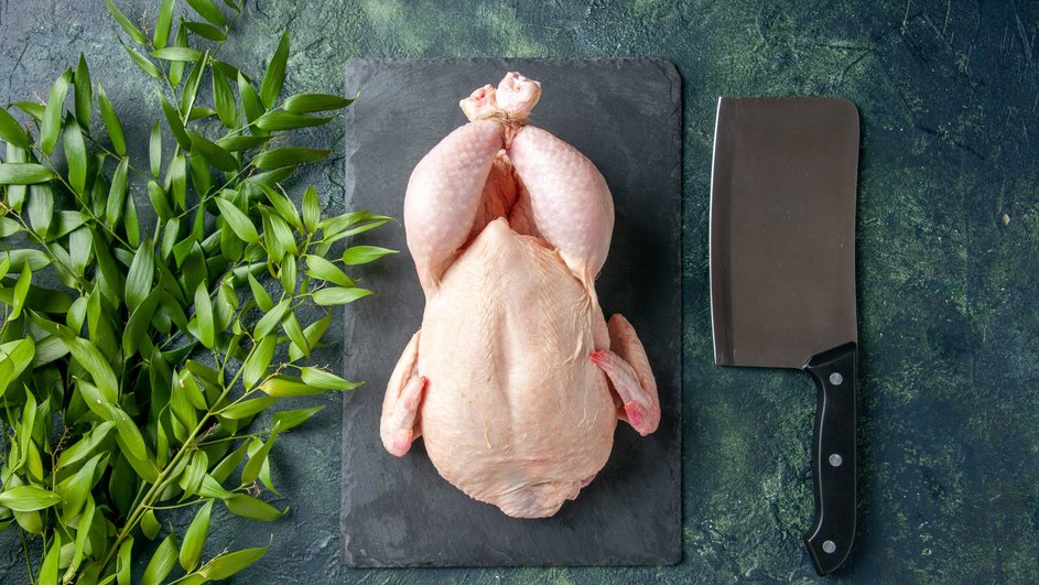 Сырая целая курица лежит на подставке рядом с ножом