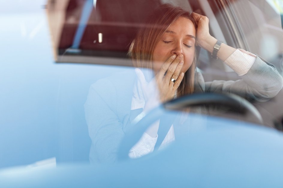 Женщина чувствует усталость и зевает за рулем автомобиля. Вид сквозь стекло.