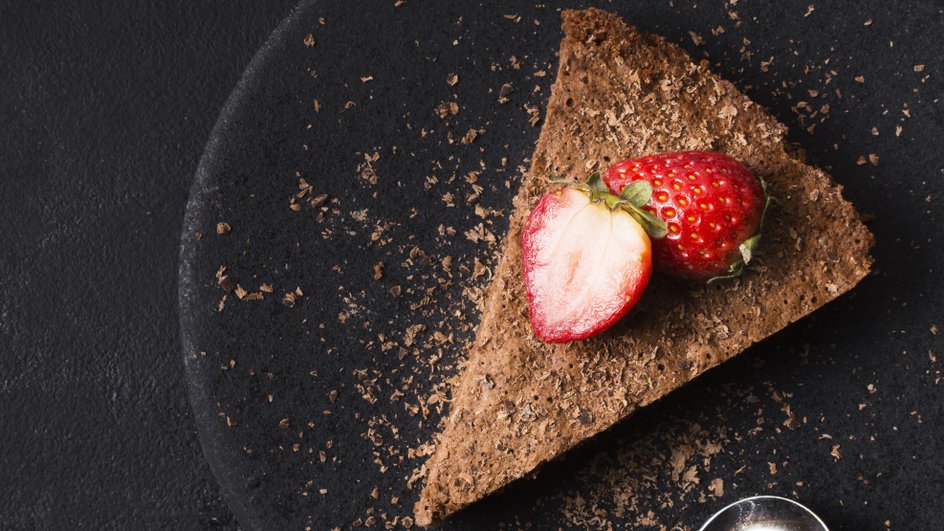 Кусочек торта «Три шоколада» лежит на тарелке с клубникой Кусочек торта «Три шоколада» лежит на тарелке с клубникой
