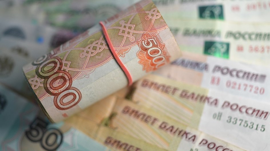 Пятитысячные банкноты обтянуты оранжевой резинкой на фоне бумажных рублей
