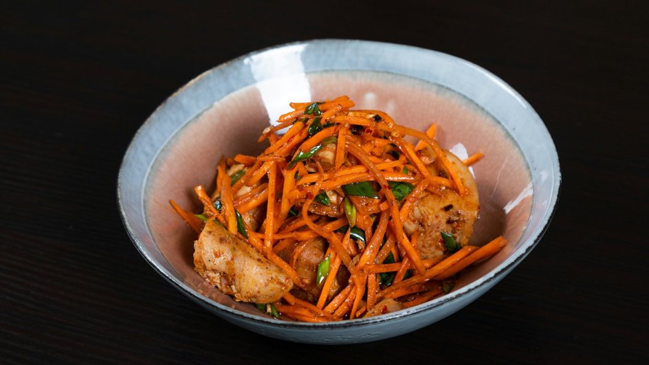 Салат с корейской морковью и куриной печенью лежит на тарелке