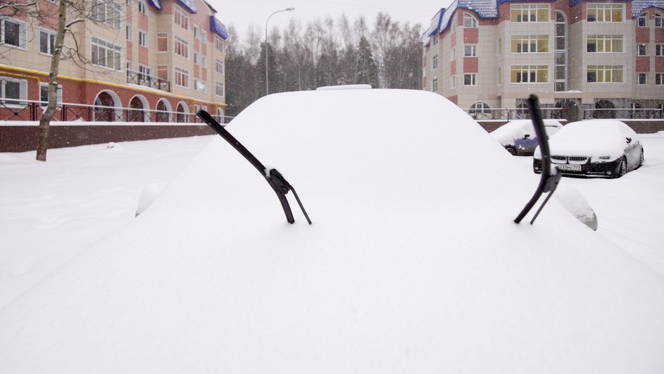 Автомобиль полностью покрыт снегом на парковке около дома