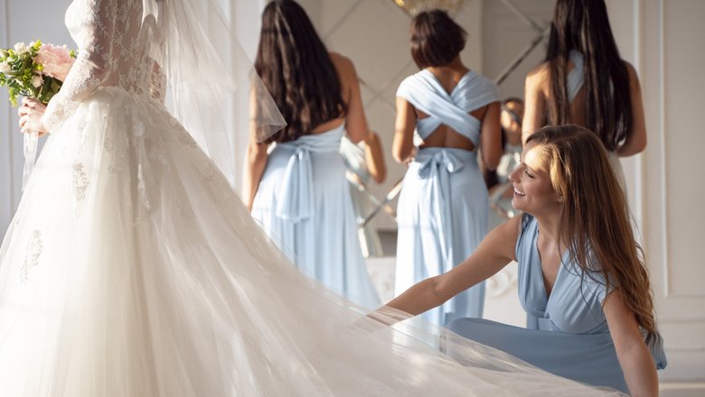 Подружка невесты держит шлейф платья