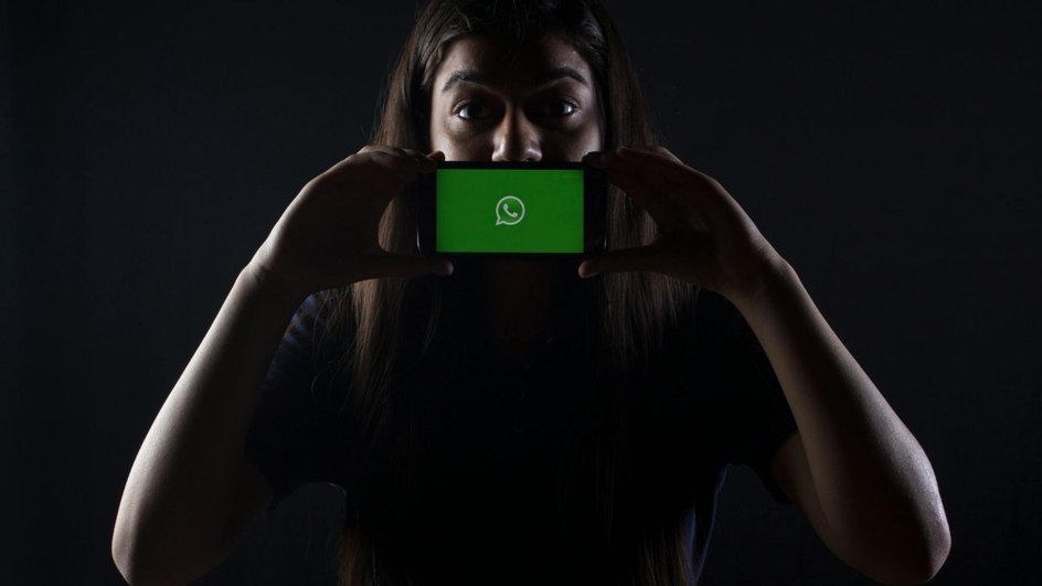 Девушка держит телефондвумя руками перед лицом, на экране смартфона открыт логотип WhatsApp Девушка держит телефондвумя руками перед лицом, на экране смартфона открыт логотип WhatsApp