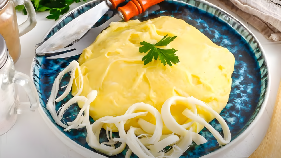 Грузинская кукурузная каша с сыром лежит на тарелке рядом с приборами