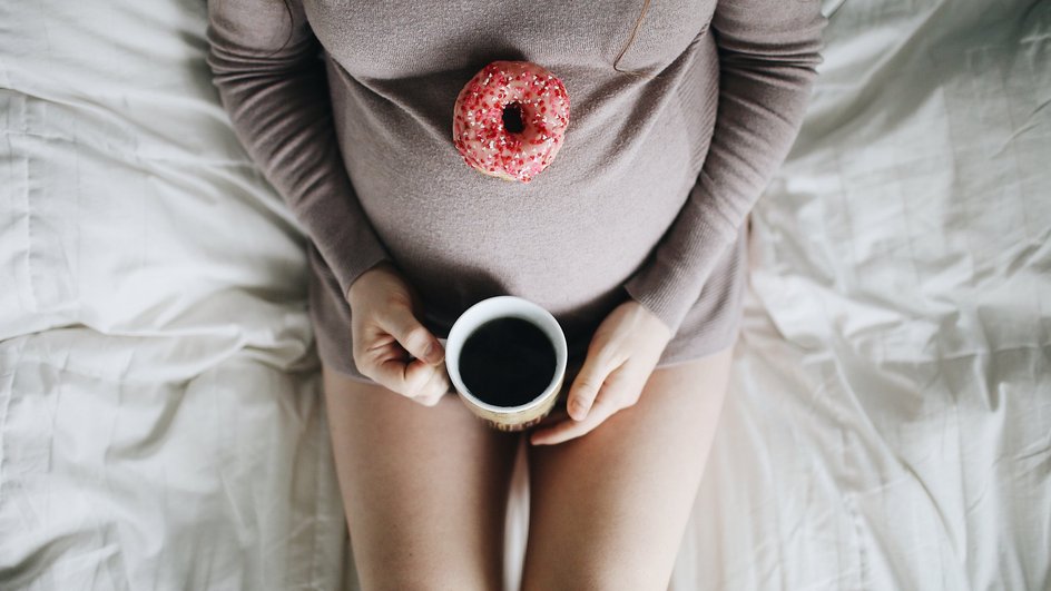 Крупным планом: беременная женщина ест пончик с чаем в постели