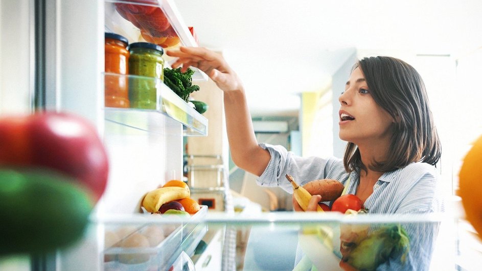 Девушка в рубашке достает продукты из двери холодильника 