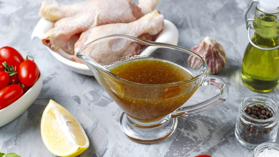Соусница с маринадом стоит на столе рядом с ингредиентами и мясом