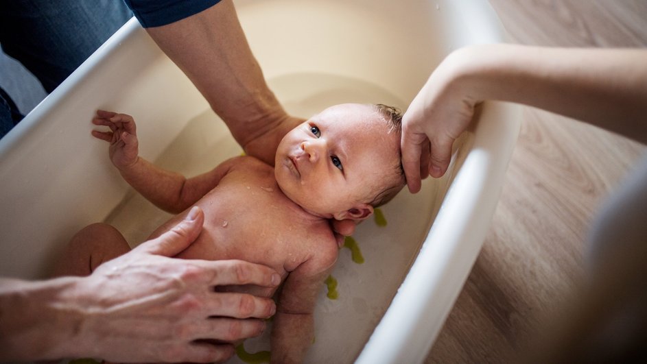Родители купают новорожденного в ванночке Родители купают новорожденного в ванночке