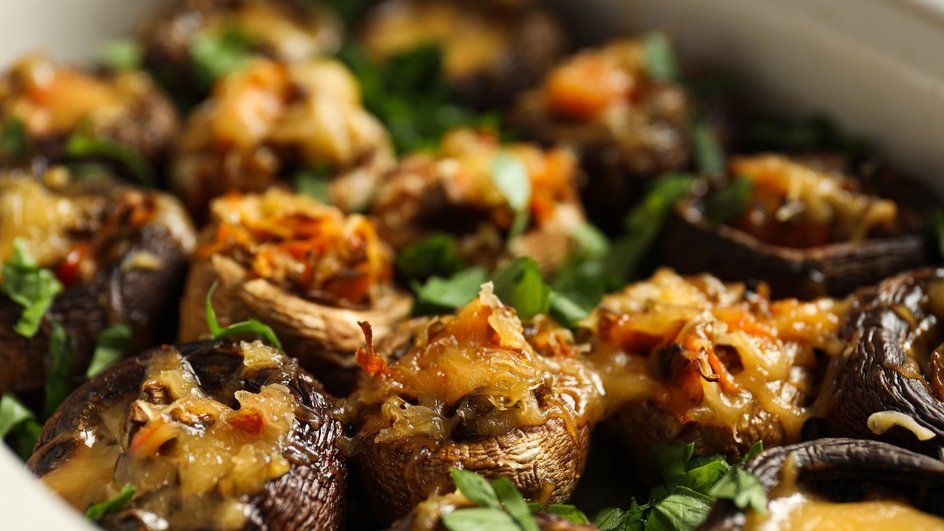 Запеченные маслята, фаршированные овощами и покрытые сыром, украшенные зеленью и поданные в белой тарелке