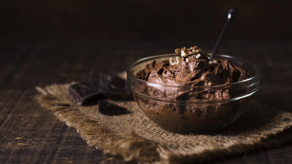 Стеклянная миска с шоколадным мороженым с соленой карамелью, украшенное орехами, на фоне темной поверхности и кусочков шоколада Стеклянная миска с шоколадным мороженым с соленой карамелью, украшенное орехами, на фоне темной поверхности и кусочков шоколада