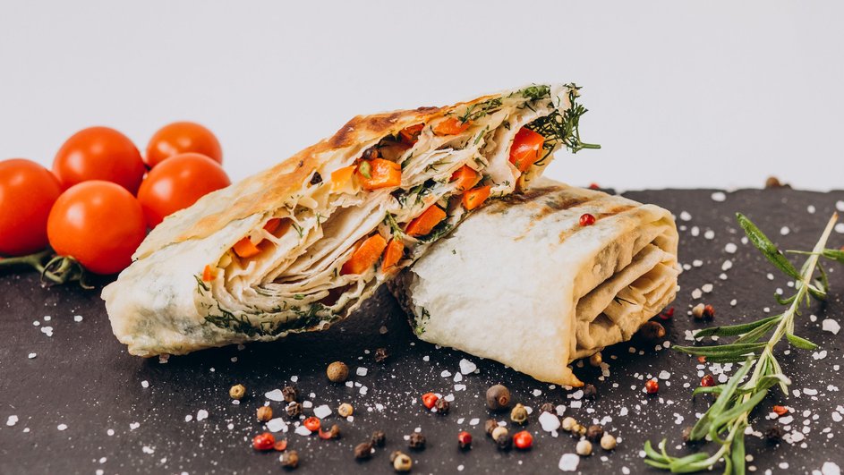Рулет из лаваша с курицей и чесночным соусом в разрезе лежит на столе рядом с ингредиентами