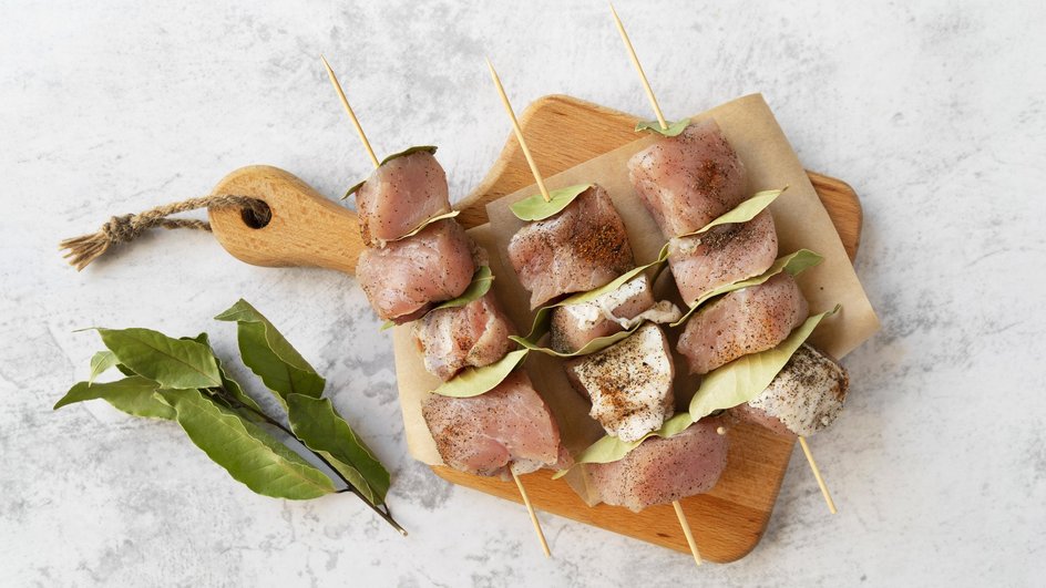 Замаринованный шашлык из курицы на шпажках лежит на разделочной доске Замаринованный шашлык из курицы на шпажках лежит на разделочной доске