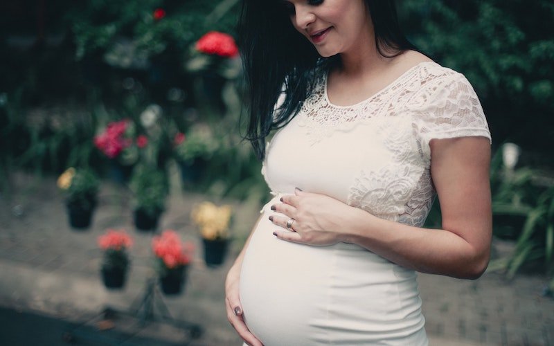 close-up-photo-of-pregnant-woman-in-white-dress-holding-her-2100341
