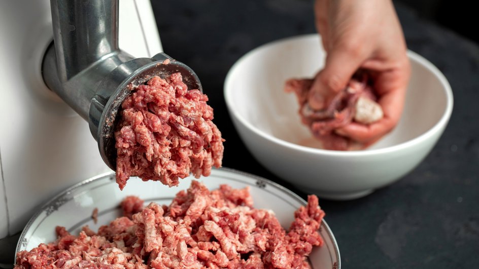 Человек прокручивает фарш через мясорубку Человек прокручивает фарш через мясорубку