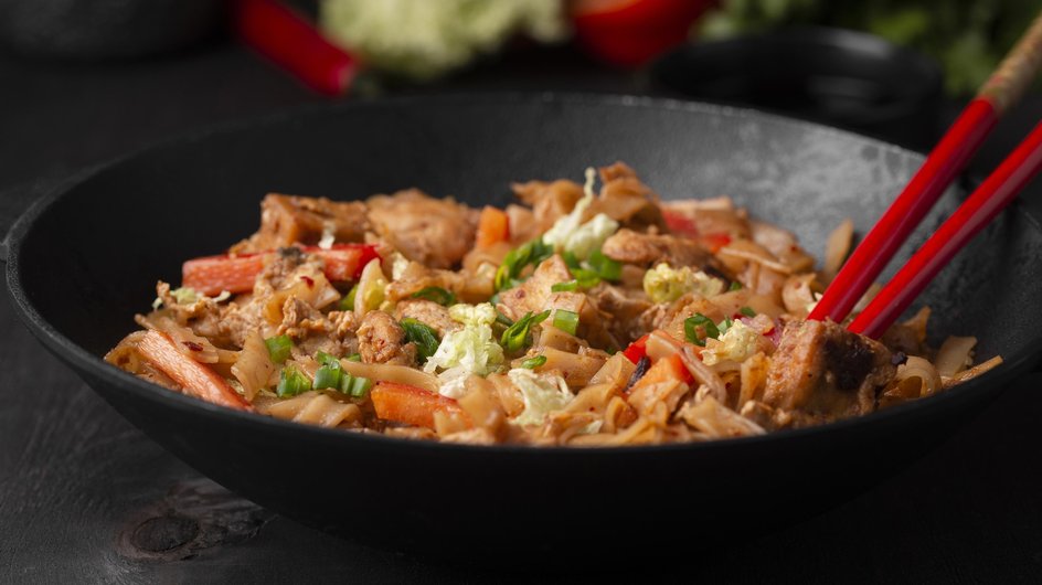 Тарелка домашней лапши вок с курицей и соусом терияки стоит на столе с палочками