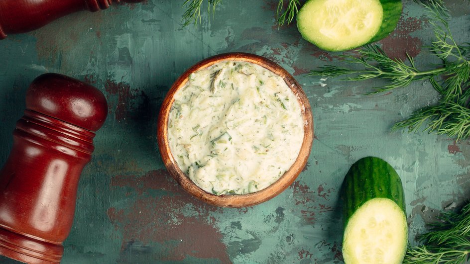 Соус тартар к красной рыбе с огурцом и укропом в деревянной пиале, рядом свежий огурец, укроп и перцемолка
