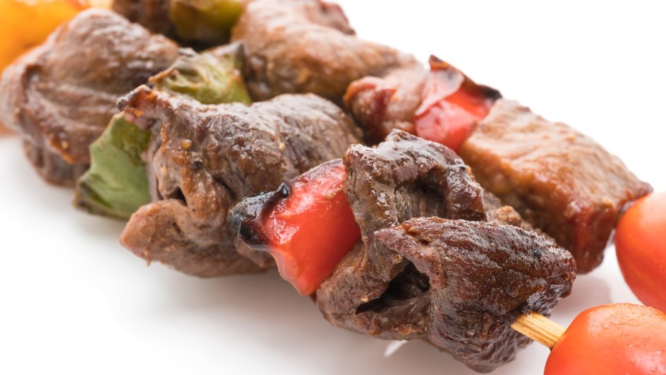 Шашлык на шпажках с мясом из говядины, перцем и помидорами лежит на белой тарелке Шашлык на шпажках с мясом из говядины, перцем и помидорами лежит на белой тарелке
