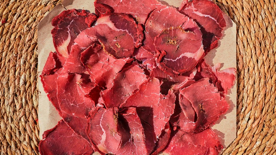Мясные чипсы (Джерки) выложены на салфетку на плетенной подставке Мясные чипсы (Джерки) выложены на салфетку на плетенной подставке