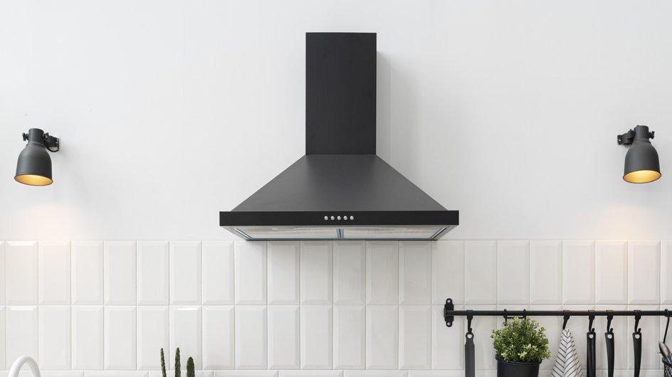 Черная кухонная вытяжка на фоне белой плитке с лампочками по бокам 