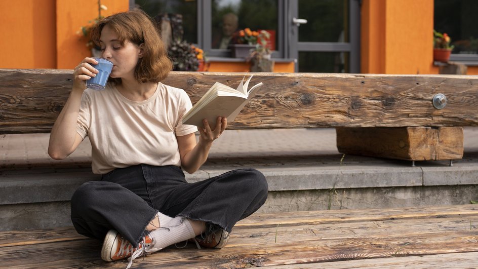 Женщина читает книгу на веранде и пьет из стакана Женщина читает книгу на веранде и пьет из стакана
