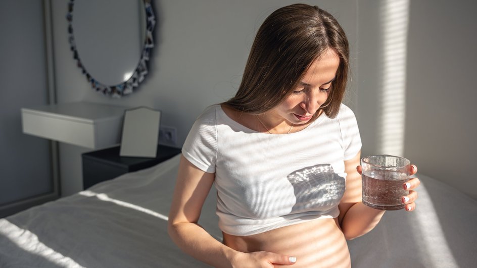 Беременная женщина пьет воду сидя на кровати