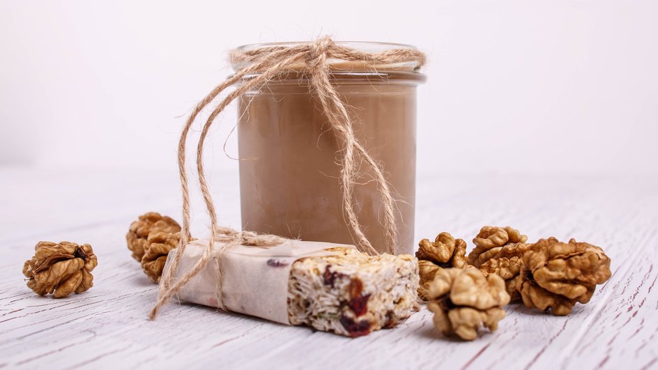 Открытая банка ореховой пасты стоит на столе рядом с грецкими орехами и батончиком
