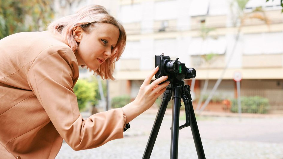 Девушка настраивает фотоаппарат на штативе на улице