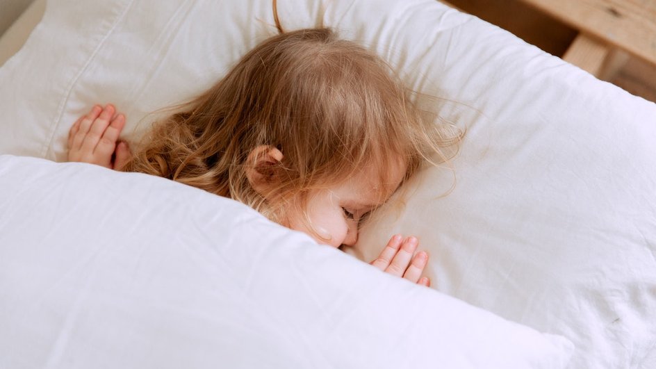 Ребенок спит на белой подушке укрытый белым одеялом