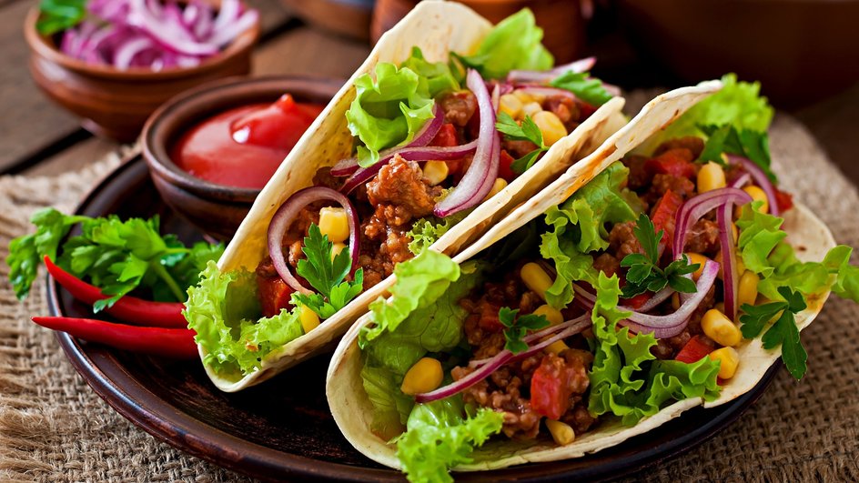 Тако из куриного фарша и кукурузы лежит на тарелке рядом с кетчупом Тако из куриного фарша и кукурузы лежит на тарелке рядом с кетчупом