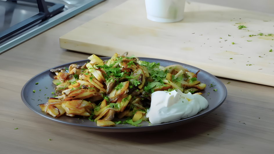 Картошка с вешенками, украшенная зеленью и сметаной, на тарелке Картошка с вешенками, украшенная зеленью и сметаной, на тарелке
