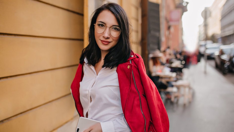 Женщина-Лев в очках стоит на улице и держит телефон в руке Женщина-Лев в очках стоит на улице и держит телефон в руке