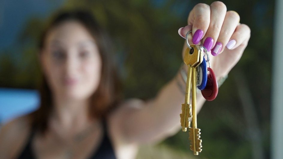 Девушка держит ключи от квартиры на вытянутой руке