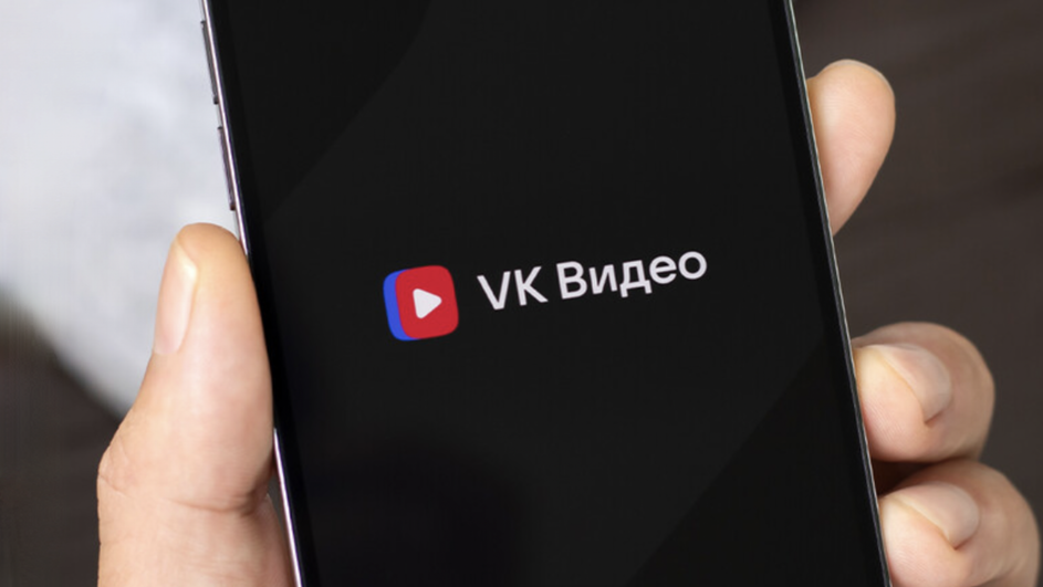 Человек держит в руке телефон, на котором горит логотип VK Видео, где можно смотреть онлайн-трансляции