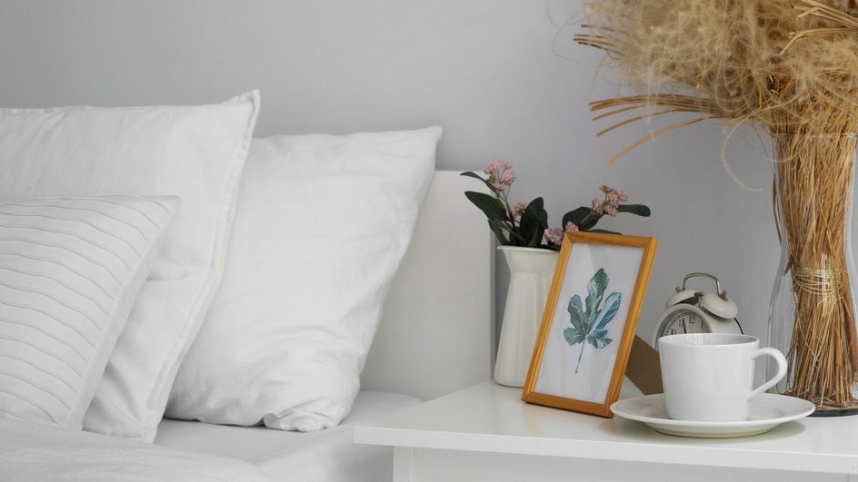 Спальня с белыми подушками, фоторамкой и чашкой на прикроватном столике