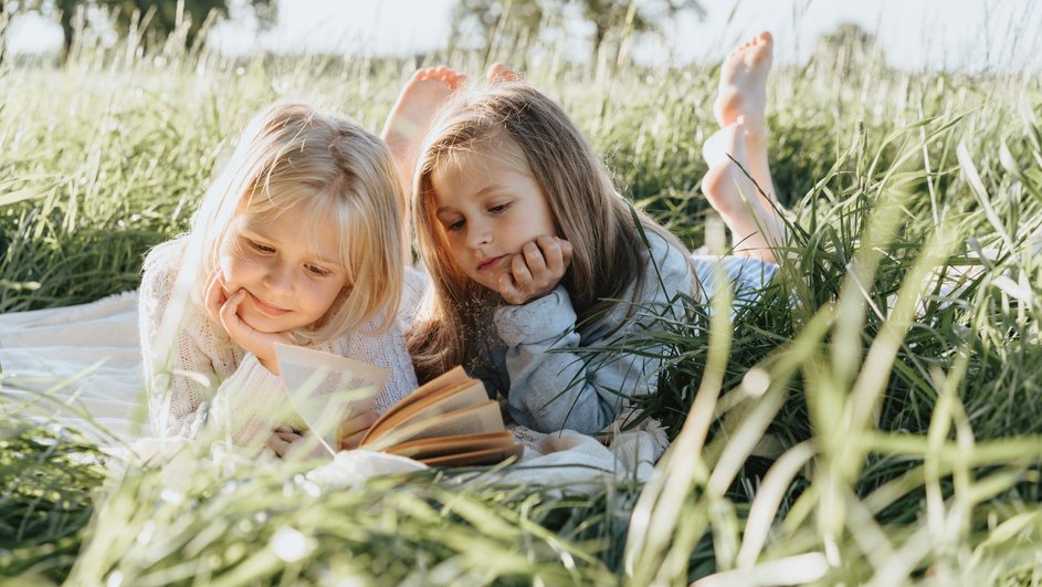 девочки читают книжку лежа на траве
