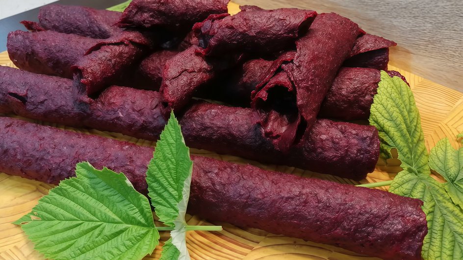 Натуральная пастила из вишни и банана без сахара в дегидраторе, закрученная в трубочки лежит на деревянной доске с листиками мяты Натуральная пастила из вишни и банана без сахара в дегидраторе, закрученная в трубочки лежит на деревянной доске с листиками мяты