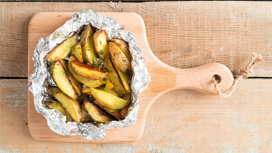 Запеченный картофель в фольге лежит на доске Запеченный картофель в фольге лежит на доске