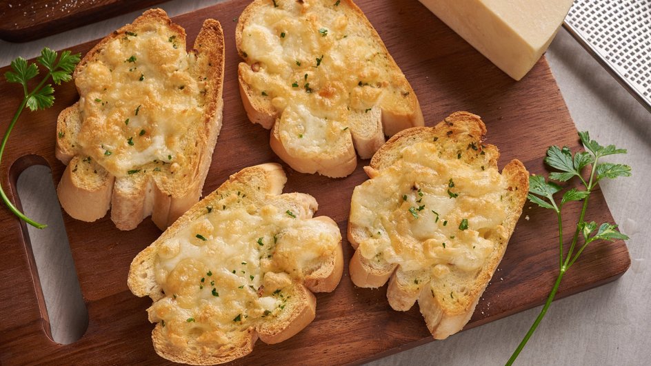 Гренки с сыром лежат на доске рядом с зеленью